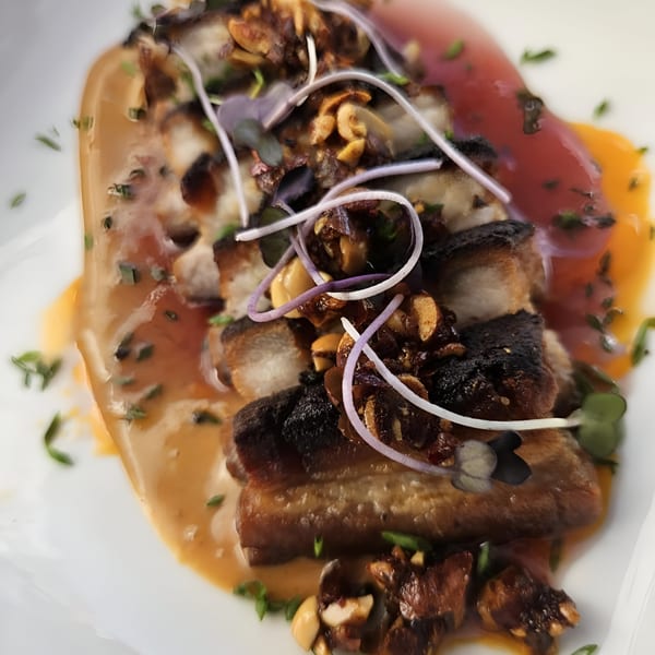 Crispy pork belly with a rich sauce, garnished with microgreens and nuts, from Recess Southern Gastro Pub.