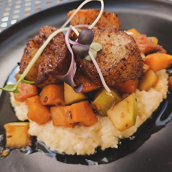 Seared scallops on a bed of grits with diced butternut squash and apples, garnished with microgreens.