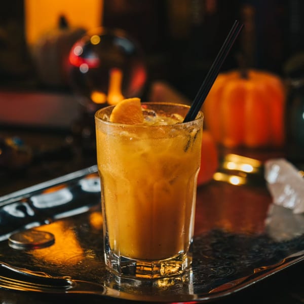 A vibrant orange cocktail with an orange slice and black straw, on a silver tray.