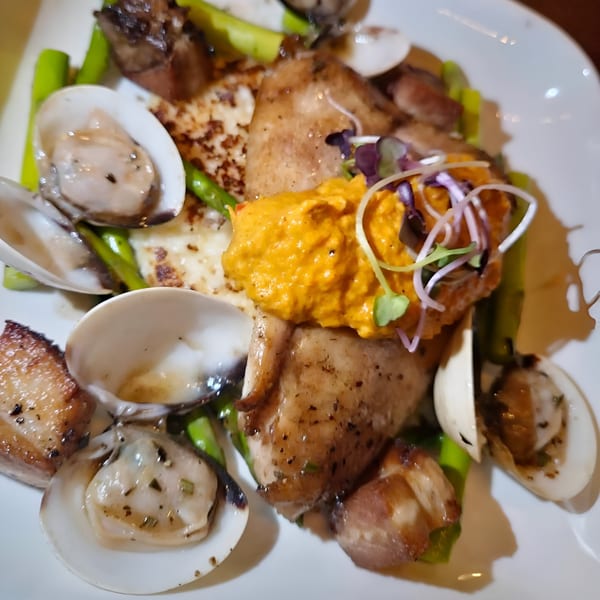 Southern-style dish with chicken, clams, asparagus, and a vibrant orange sauce on a white plate.