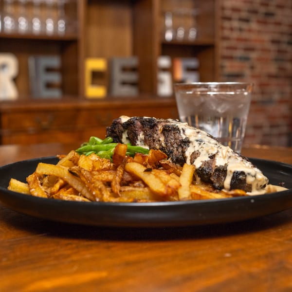 Recess Southern Gastro Pub's steak with creamy sauce, french fries, and green beans on a black plate.