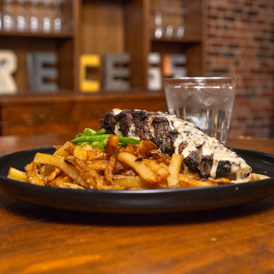 Recess Southern Gastro Pub's steak with creamy sauce, french fries, and green beans on a black plate.