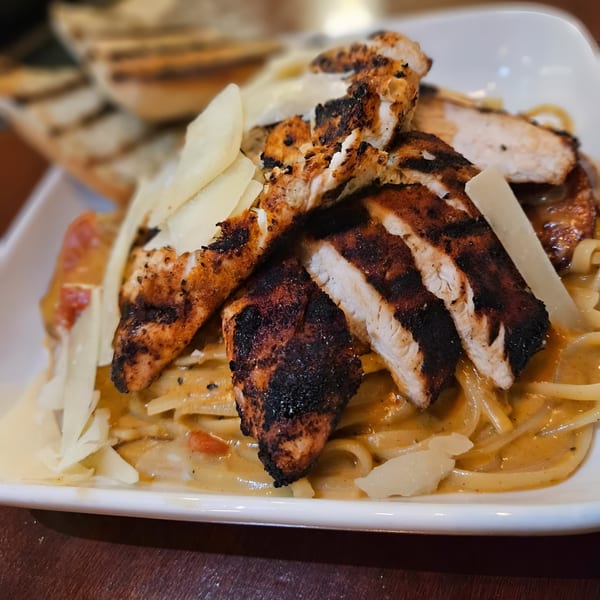 Grilled chicken and linguine pasta with creamy sauce and shaved parmesan cheese, served with grilled bread.