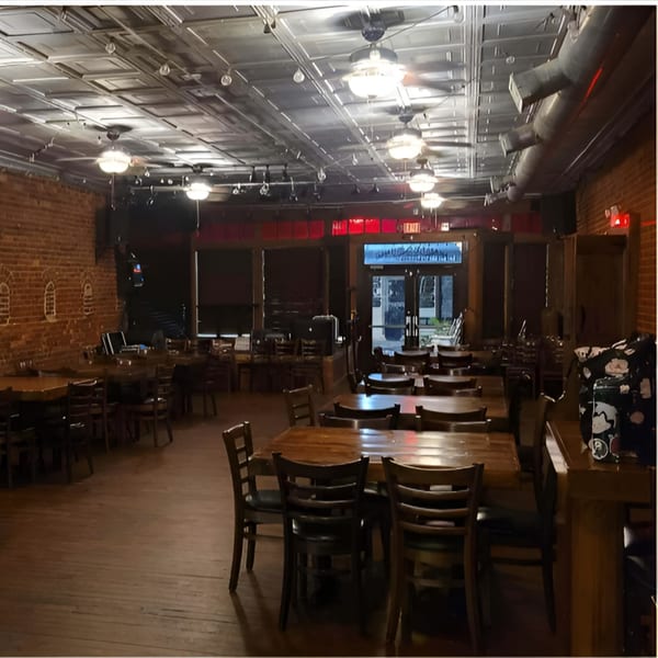 The interior of Recess Southern Gastro Pub, featuring wooden tables and chairs, brick walls, and a tin ceiling.